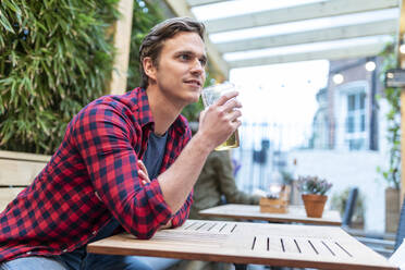 Mann schaut weg, während er am Tisch sitzt und ein Bierglas hält - WPEF04859