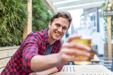 Smiling man showing beer glass at pub - WPEF04860