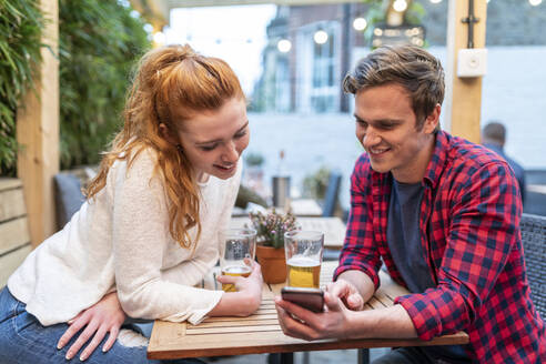Paar schaut auf sein Smartphone, während es in einer Kneipe Bier trinkt - WPEF04862