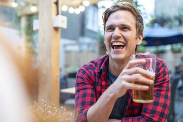 Mann lacht, während er in einer Kneipe ein Bierglas hält - WPEF04863