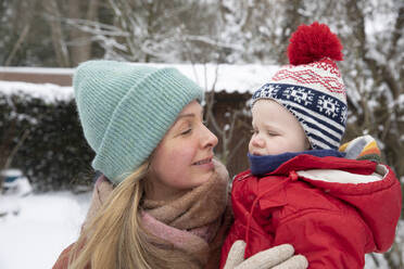 Lächelnde Mutter sieht ihren Sohn an, während sie im Hinterhof im Schnee steht - FVDF00225