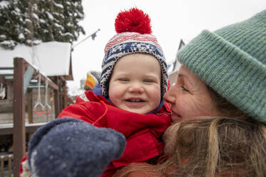 Smiling woman looking at cheerful son while standing at backyard during winter - FVDF00226
