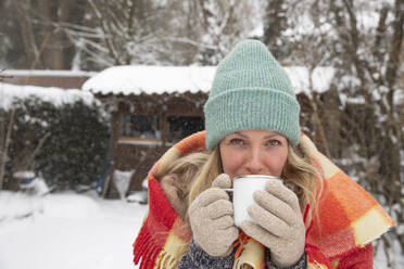 Ältere Frau mit Strickmütze trinkt Kaffee im Hinterhof bei Schnee - FVDF00228