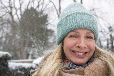 Smiling beautiful blond woman wearing knit hat during snow - FVDF00231