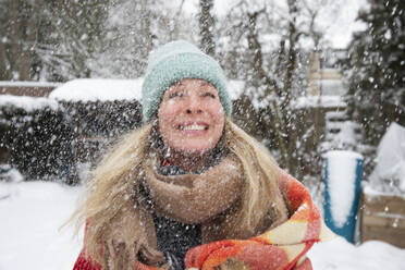 Fröhliche reife Frau mit Strickmütze und Schal bei Schneefall im Winter - FVDF00232