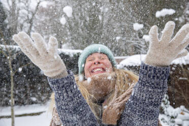 Playful woman with eyes closed throwing snow at backyard - FVDF00237