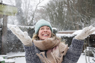 Verspielte reife Frau, die im Winter Schnee in den Hinterhof wirft - FVDF00238