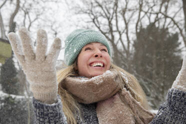 Cheerful blond woman throwing snowing while playing during winter - FVDF00240