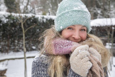 Blonde Frau bedeckt den Mund mit einem Schal, während sie bei Schnee im Hinterhof steht - FVDF00243