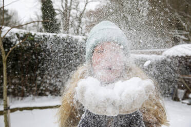 Verspielte reife Frau, die im Winter im Hinterhof steht und Schnee bläst - FVDF00244
