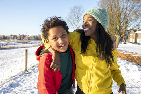 Cheerful woman with arm around son standing in snow - FVDF00255