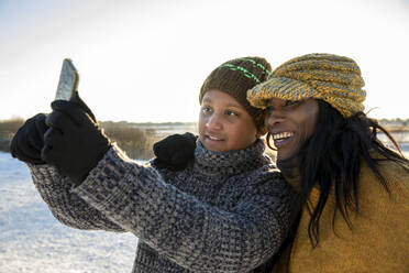 Lächelnde Frau, die im Winter ein Selfie mit ihrem Sohn per Smartphone macht - FVDF00265