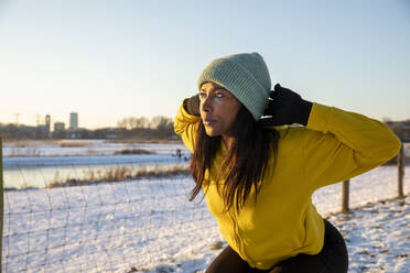 Woman with hands behind head practicing squats during winter - FVDF00274