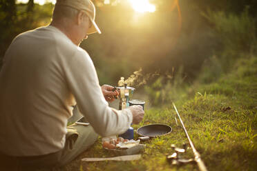 Mann macht Pause vom Fliegenfischen und kocht Kaffee am Flussufer - CAIF30668