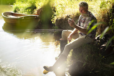 Mann mit Smartphone beim Fliegenfischen am sonnigen Fluss - CAIF30670