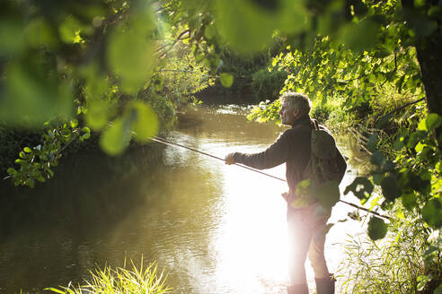 Man fly fishing at sunny idyllic summer riverbank - CAIF30671