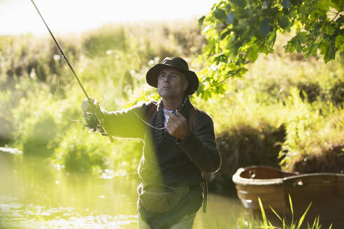 Focused man casting fly fishing pole in sunny river - CAIF30690