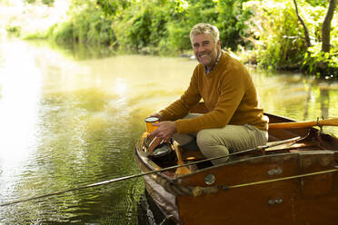 Portrait glücklicher Mann mit Kaffee Fliegenfischen in Boot auf Fluss - CAIF30700