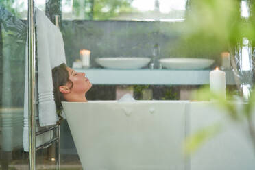 Serene woman enjoying bubble bath in modern luxury bathroom - CAIF30708