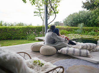 Affectionate couple cuddling on cushions on luxury patio - CAIF30717