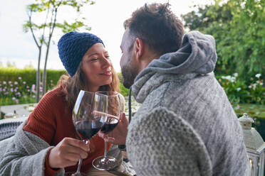 Affectionate romantic couple drinking red wine on patio - CAIF30726