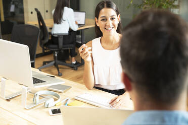 Smiling businesswoman talking with businessman at desk in office - CAIF30735