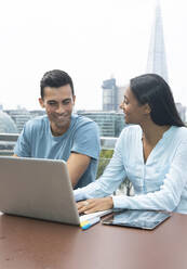 Smiling business people working at laptop on urban balcony, London, UK - CAIF30743