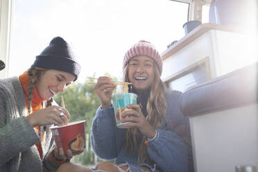 Porträt glücklicher junger Frauen, die in einem Wohnmobil Instantnudeln essen - CAIF30754