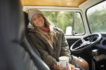Porträt einer glücklichen jungen Frau, die am Lenkrad eines Lieferwagens Kaffee trinkt - CAIF30756
