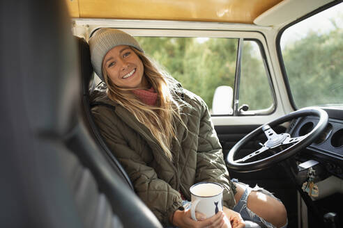 Porträt einer glücklichen jungen Frau, die am Lenkrad eines Lieferwagens Kaffee trinkt - CAIF30756