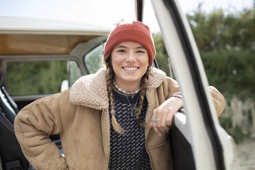 Porträt einer glücklichen jungen Frau mit Strickmütze am Eingang eines Wohnmobils - CAIF30759