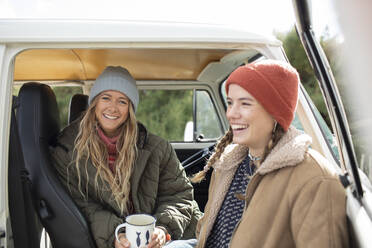 Glückliche junge Frauen, die sich mit Kaffee in der Tür eines Wohnmobils anfreunden - CAIF30760