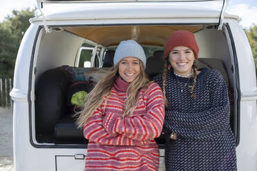 Porträt glücklicher junger Freundinnen mit Strickmützen auf der Rückseite eines Wohnmobils - CAIF30762