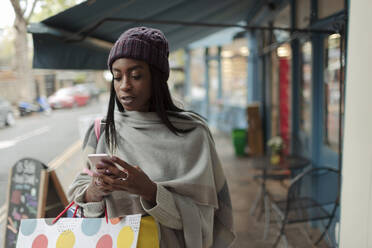 Junge Frau mit Smartphone und Einkaufstüten auf dem Bürgersteig - CAIF30774
