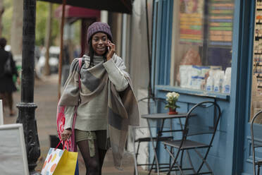 Junge Frau mit Einkaufstasche, die in einem Geschäft mit ihrem Smartphone telefoniert - CAIF30775