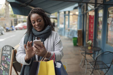 Woman with smart phone and shopping bags on sidewalk - CAIF30779