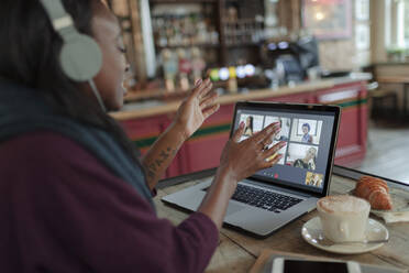 Woman video conferencing with colleagues at laptop on cafe table - CAIF30790