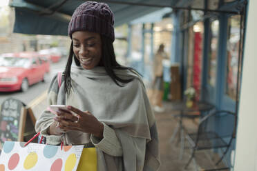 Junge Frau mit Einkaufstasche und Smartphone auf dem Gehweg - CAIF30798