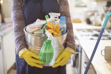 Woman holding bucket of cleaning supplies in kitchen - CAIF30816