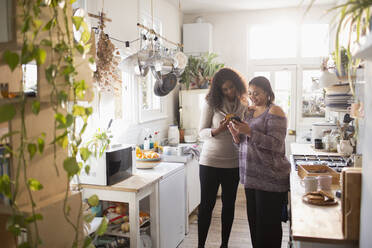 Mother and daughter using smart phone in kitchen - CAIF30818