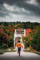 Junge läuft in Richtung einer Brücke in der Baumreihe im Herbst - CAVF94154