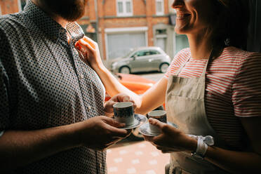 Young couple with cups of coffee smiling to each other in the street - CAVF94165