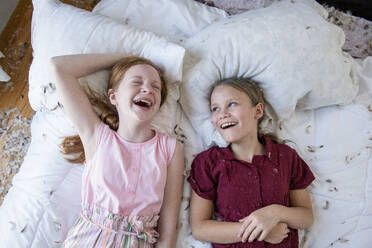 Zwei glückliche junge Mädchen, die sich auf dem Bett eine Kissenschlacht liefern. - CAVF94166