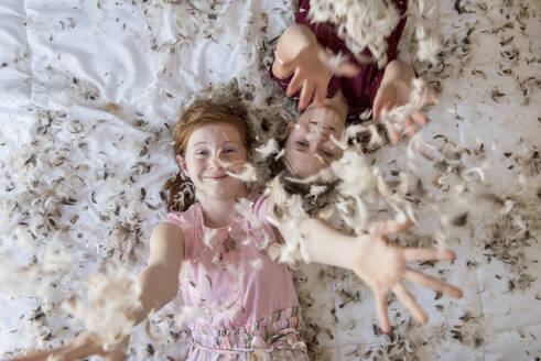 Two happy young girls having a feather pillow fight on the bed. - CAVF94169