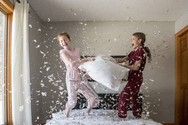 Two happy young girls having a feather pillow fight on the bed. - CAVF94170