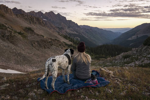 Frau betrachtet die Berge beim Wandern mit Hund bei Sonnenuntergang - CAVF94179