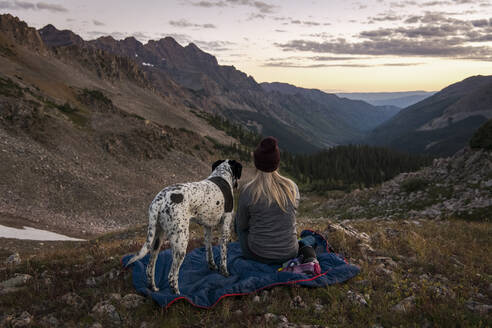 Woman looking at mountains while hiking with dog during sunset - CAVF94179