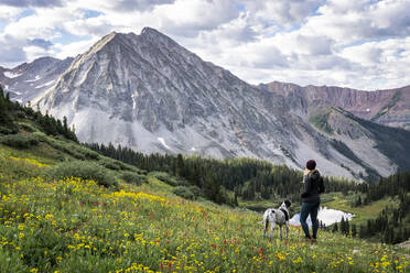 Female hiker with dog looking at view from mountain against cloudy sky - CAVF94180