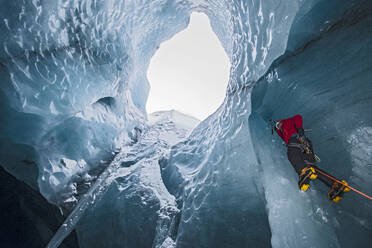 Man climbing icicle inside glacier cave in Iceland - CAVF94203