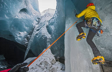 Mann klettert auf Eiszapfen in einer Gletscherhöhle in Island - CAVF94204